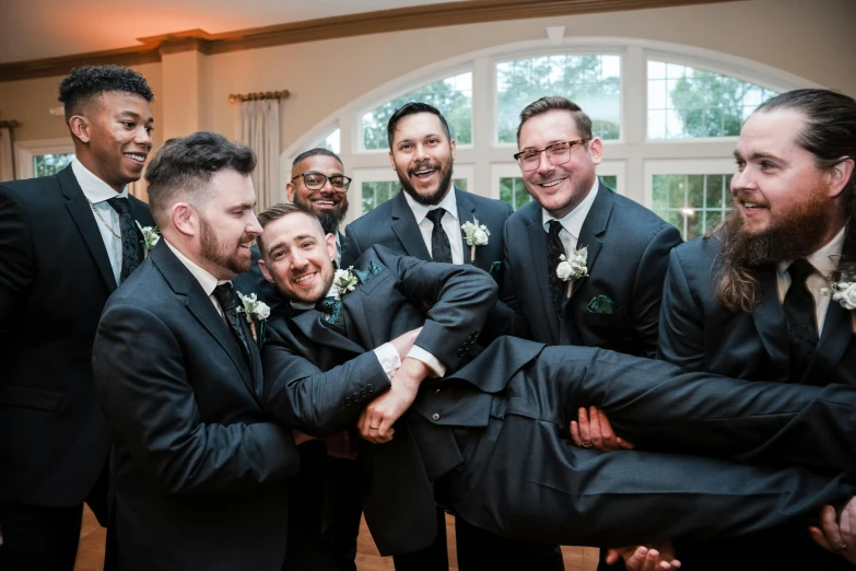 a group of grooms in suits hug and smile together