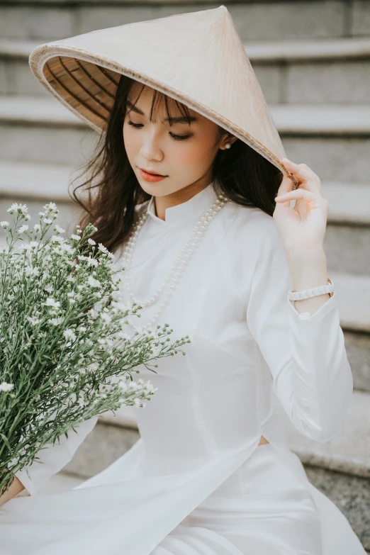 a woman in a white dress and a large hat sitting down