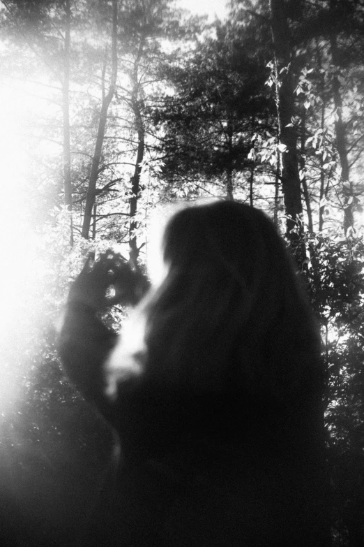 a woman walking in the woods with her light shining from the shadows
