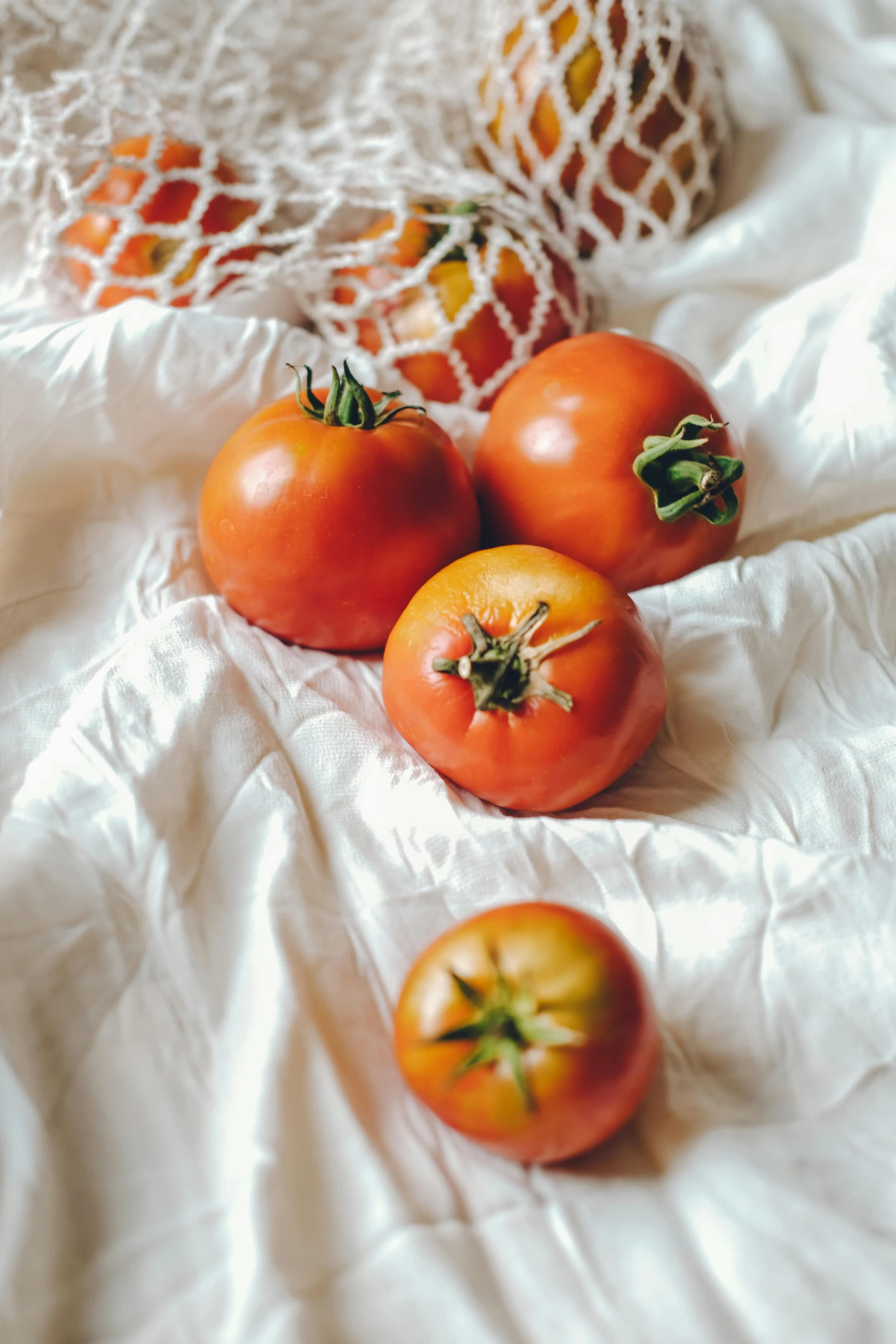 four tomatoes, one with green stem, one with red, one on white cloth