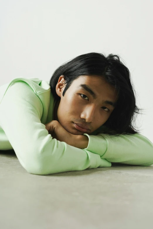 man resting on his knees with one hand on his head, his other in his other hand, and he wears an emerald sweater over a green turtle neck