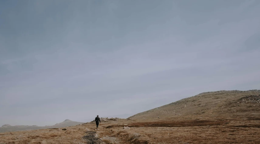 a lone person on a road leading towards a hill