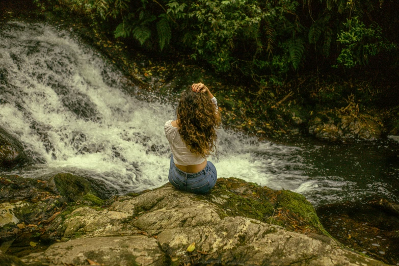 a woman sitting on top of a rock near a waterfall