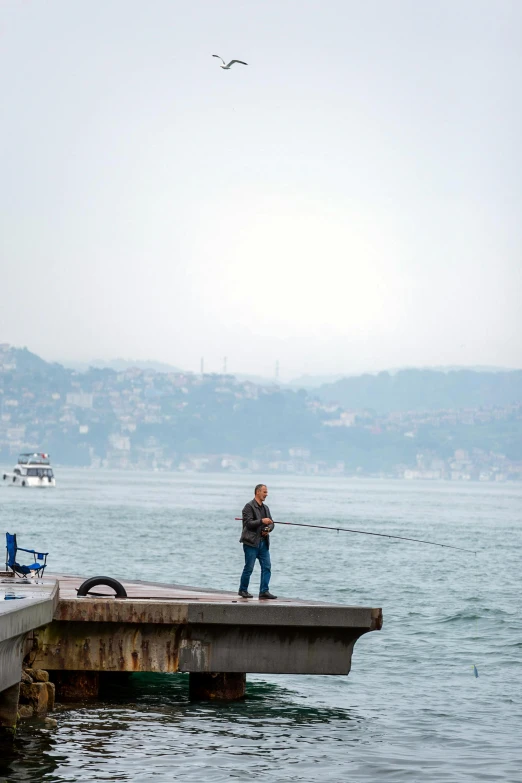 a man standing on a dock by the water with a fishing pole