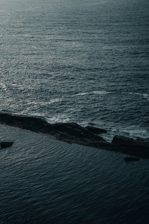 two people fishing in the ocean off a rocky beach