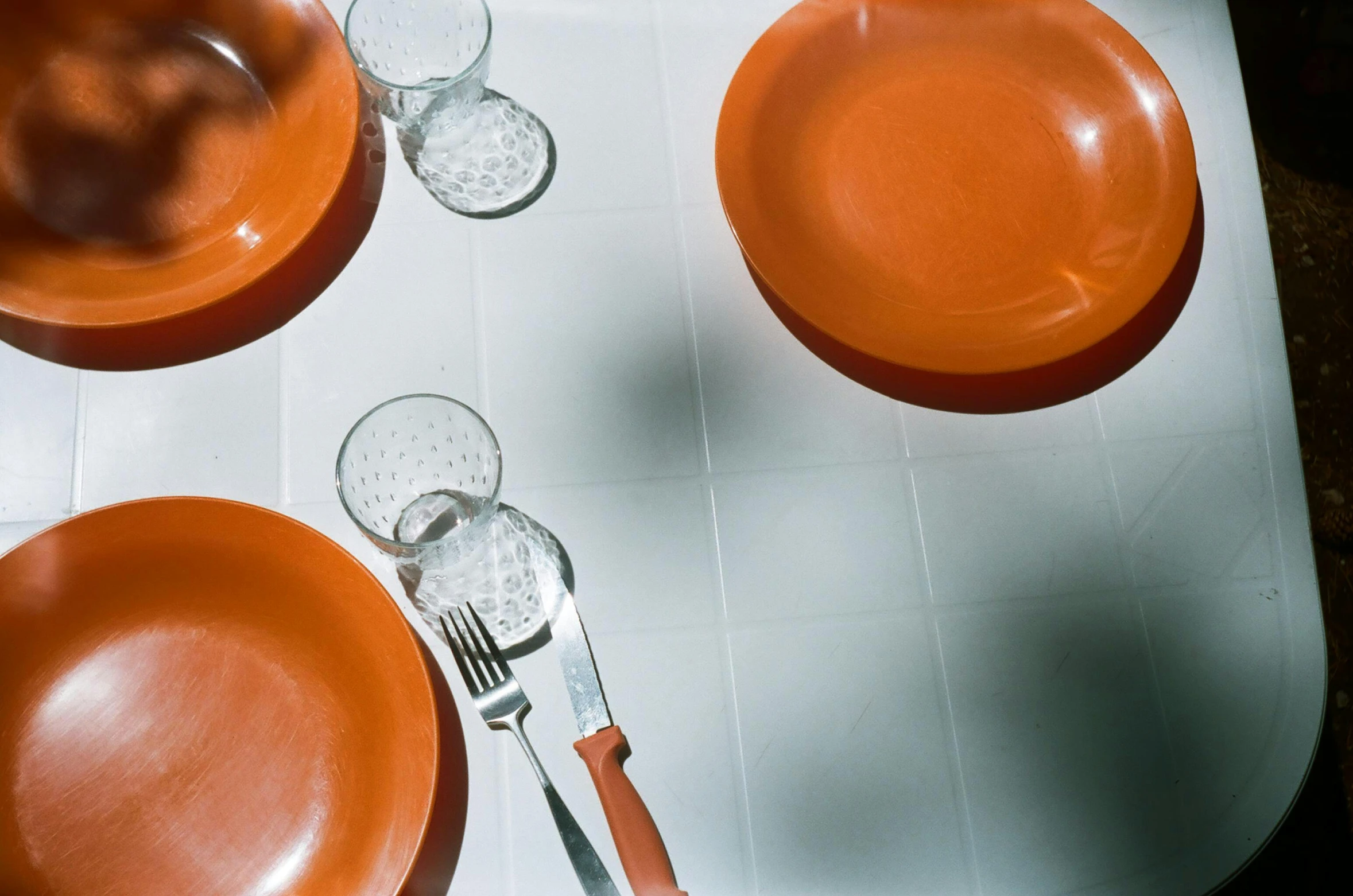 an orange table setting for four with utensils, orange plates and wine glasses