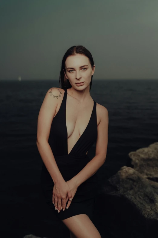 the young lady in the black dress is leaning against a rock