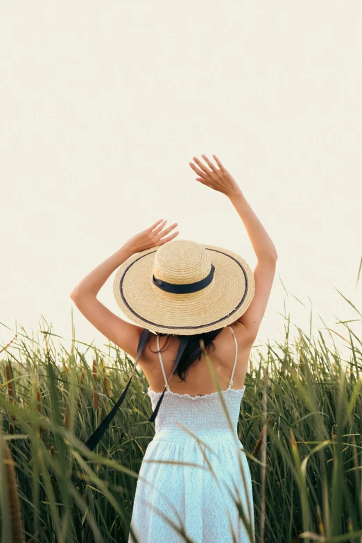 a woman standing in a field holding her hat