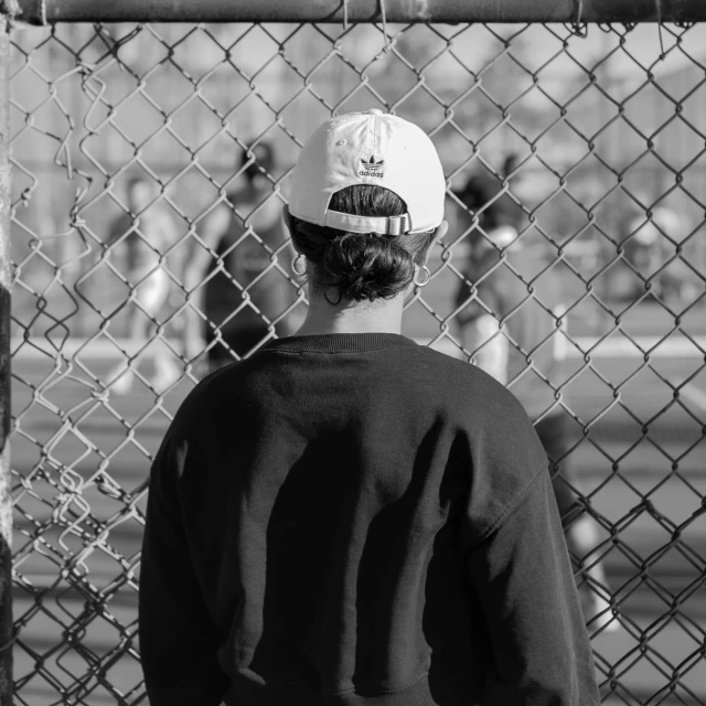 a person standing behind a fence wearing a baseball cap