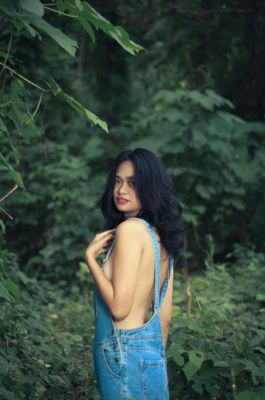 a young woman in overalls standing near a tree