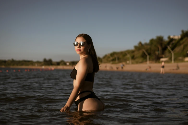 a woman in a bikini wearing sunglasses wading in a body of water