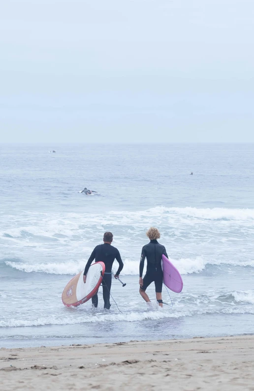 two people walking out of the ocean with surfboards