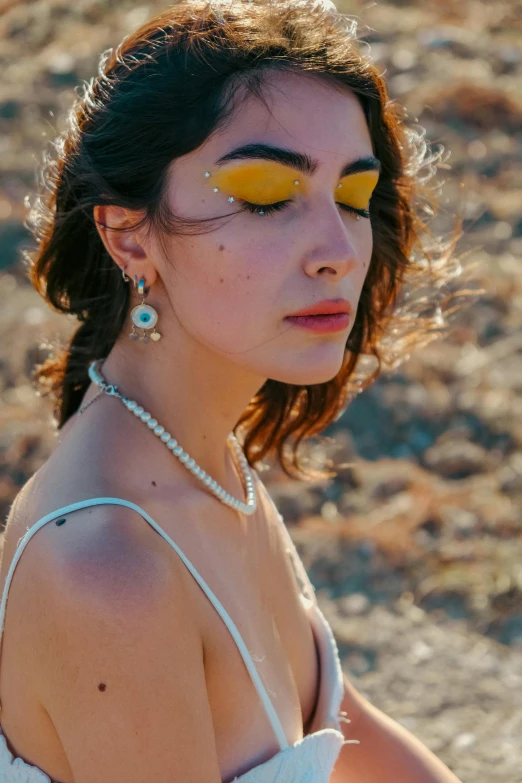 a woman with yellow makeup, wearing a white dress and earrings