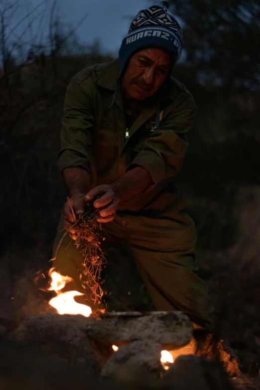 a woman crouches over a fire in the dark