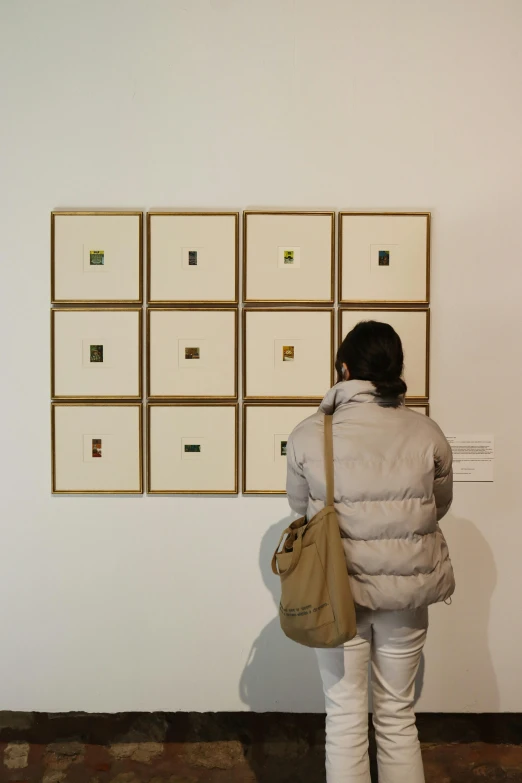 a person standing in front of a large white wall with several gold colored boxes on it