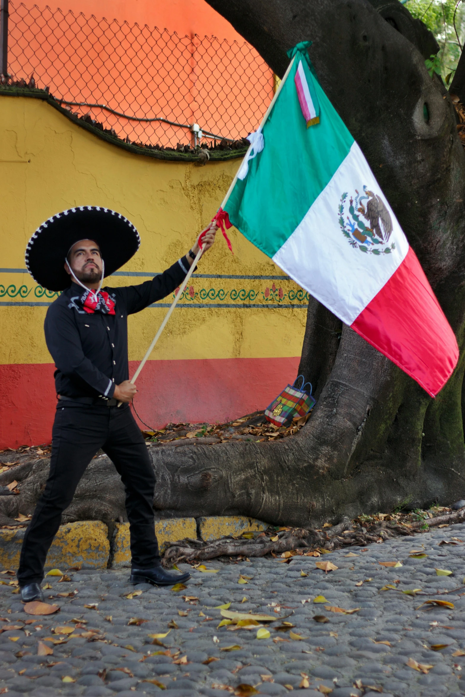 a man holding an mexico flag next to a tree