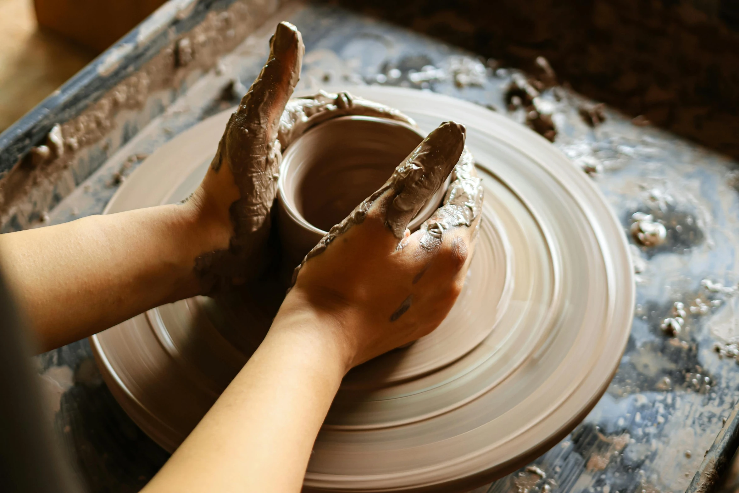 two hands hold a pottery bowl over a potter's wheel