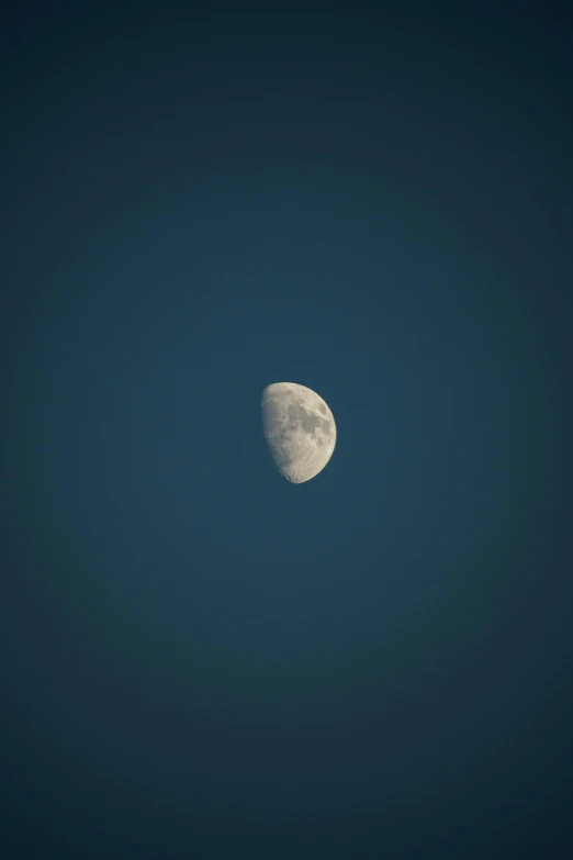 a white half moon in a clear blue sky