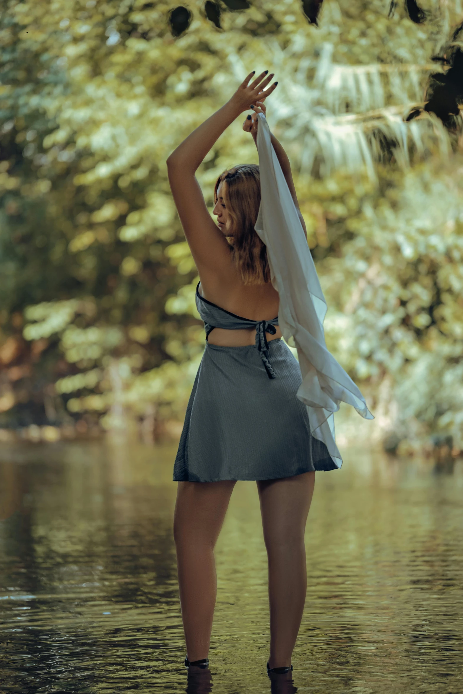 a woman wearing a grey dress standing on a riverbank