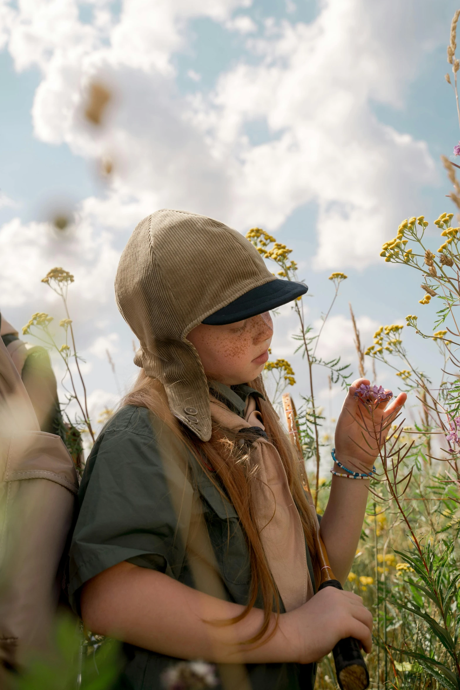 a woman in an old hat stands in a field with wild flowers