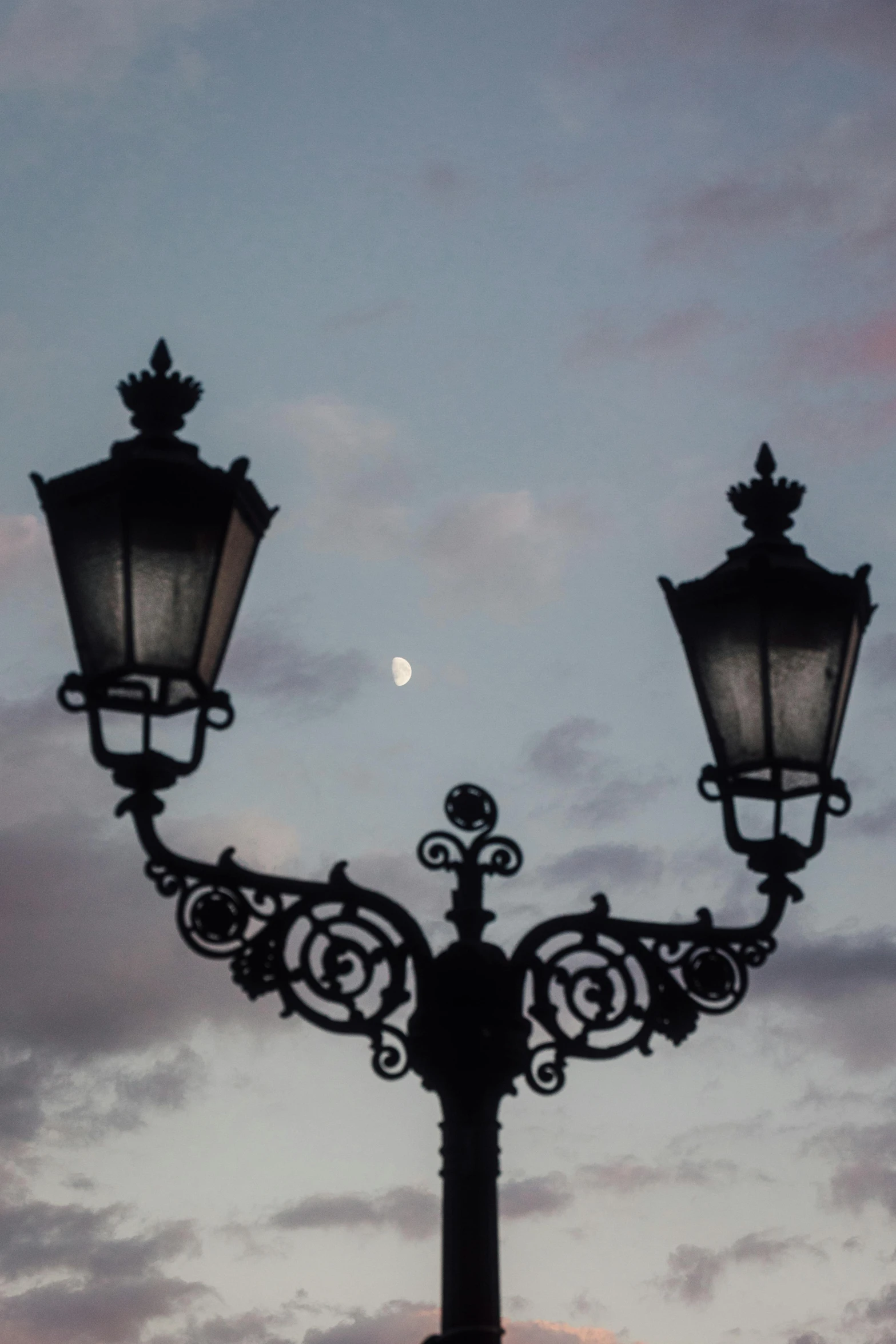 a street light at dusk with a half moon in the distance