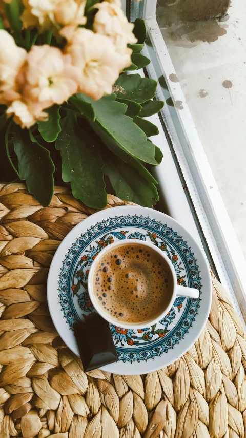 a cup of coffee sits on a wicker table beside a window