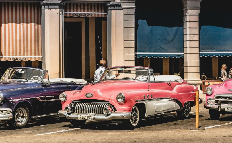 three classic cars parked side by side in a parking lot