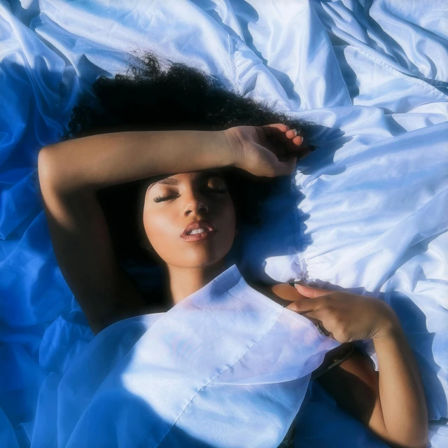 a woman laying on a bed covered in a blue blanket