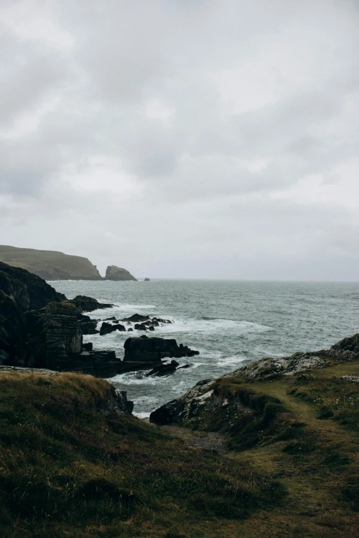 the ocean with rocks and grass under a cloudy sky