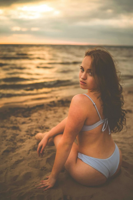 a woman sitting on top of a beach near water