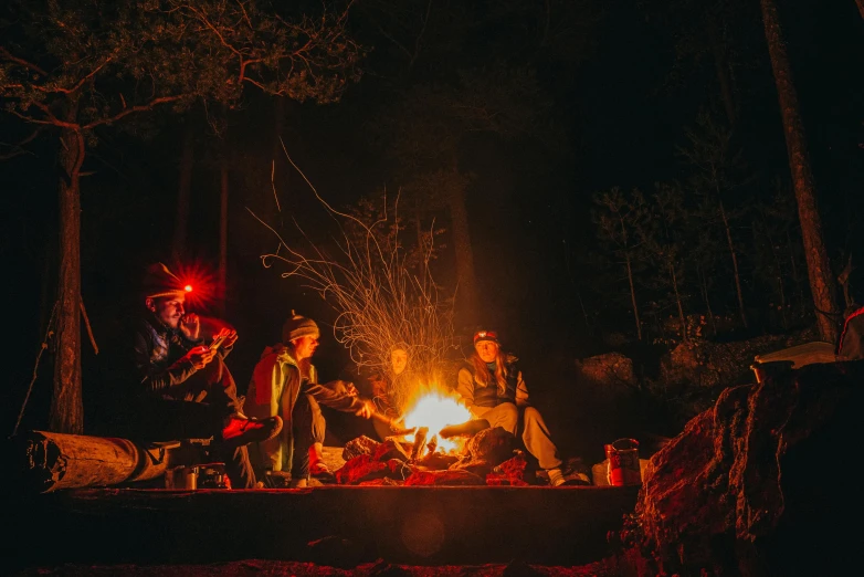 a couple sitting next to a fire in a forest