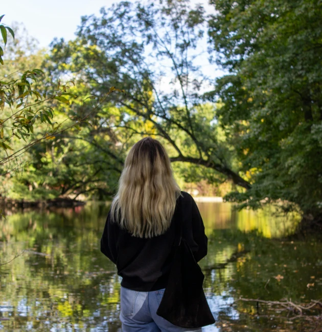 woman standing on rocks by lake staring out at trees