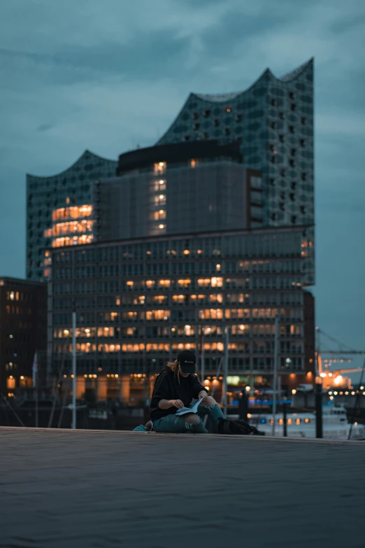 two people are sitting on the ground near water with buildings