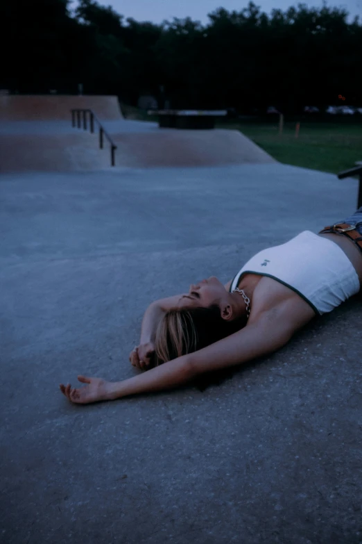 a woman in a tank top lays on the ground while holding a skateboard