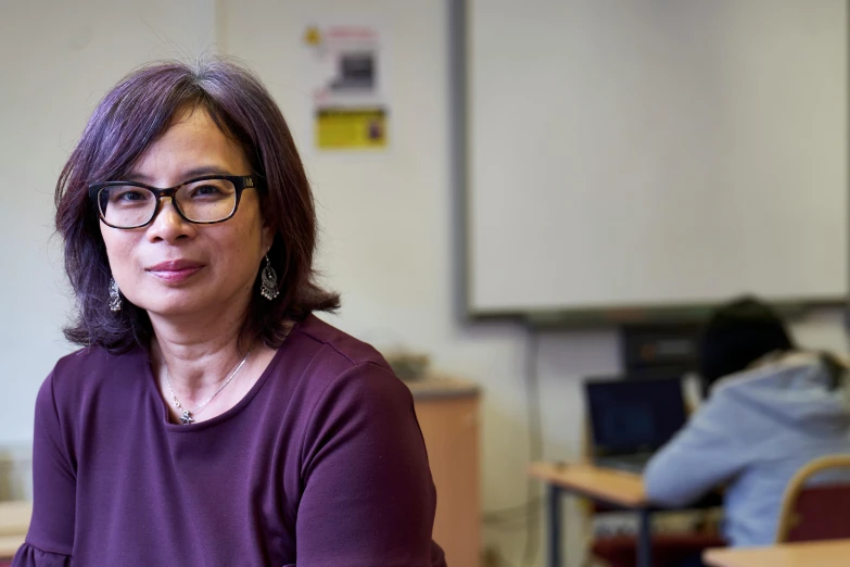 a woman wearing glasses sitting down in front of a whiteboard