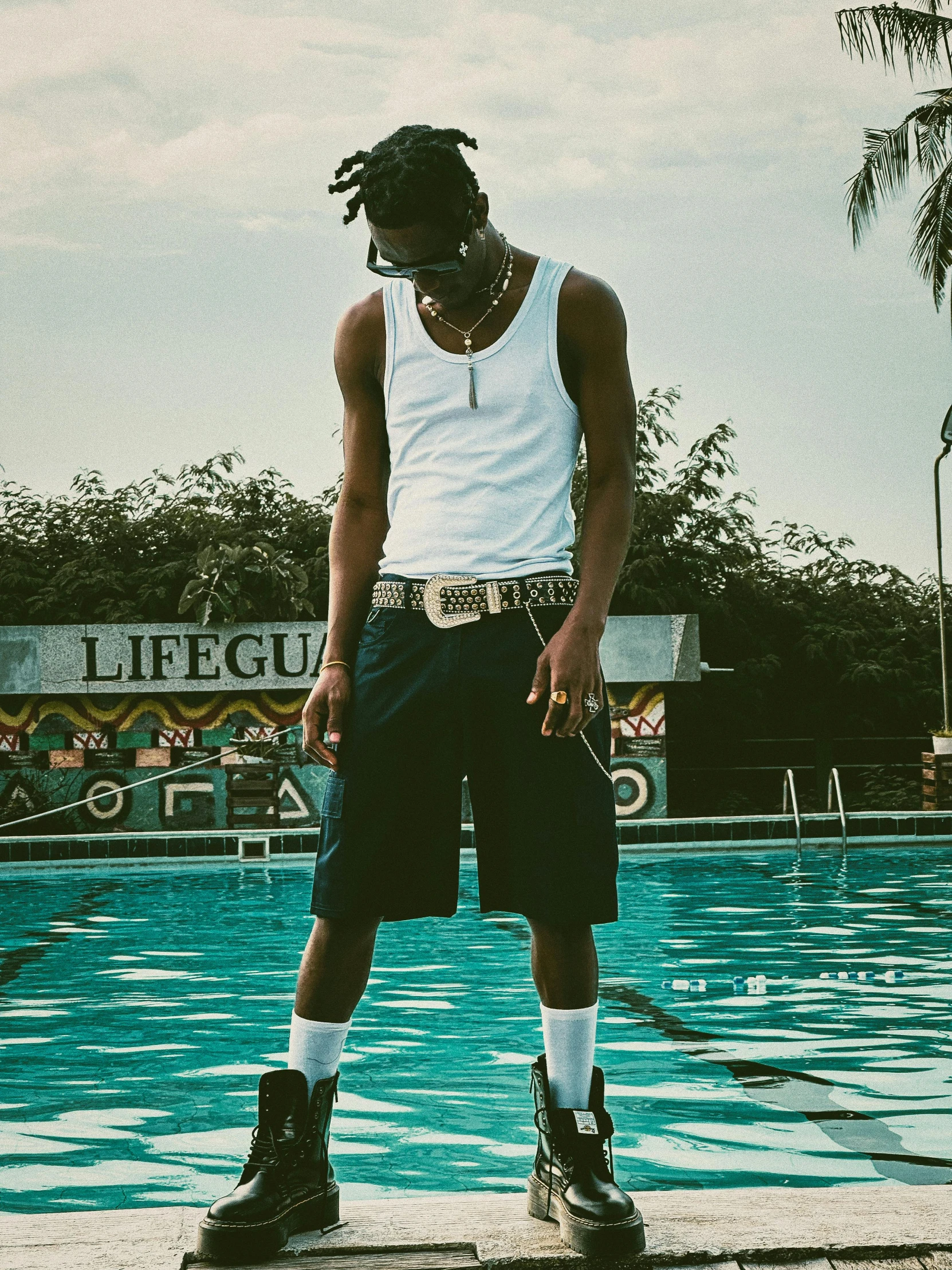 a young man standing next to a pool in front of a palm tree