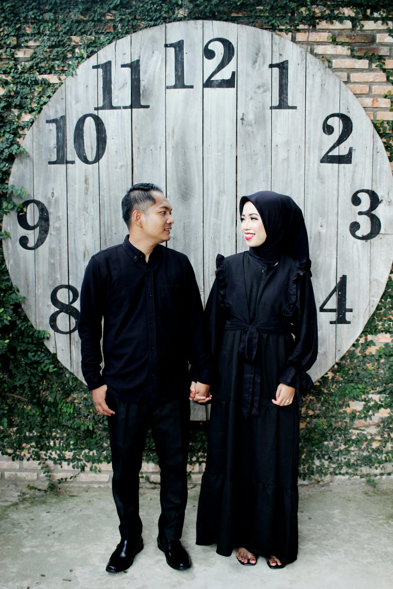 a muslim couple dressed in black standing next to a large clock