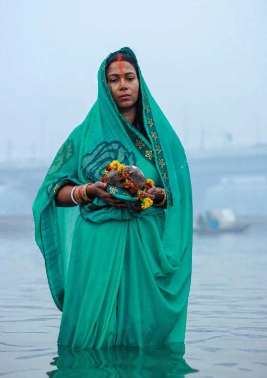 a woman standing in a lake with a flower arrangement on her hands