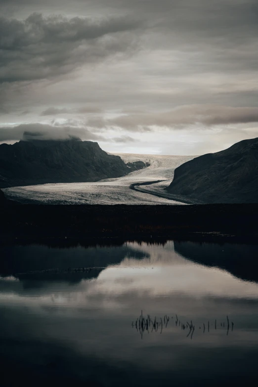 a dark and stormy day with mountains reflected in water