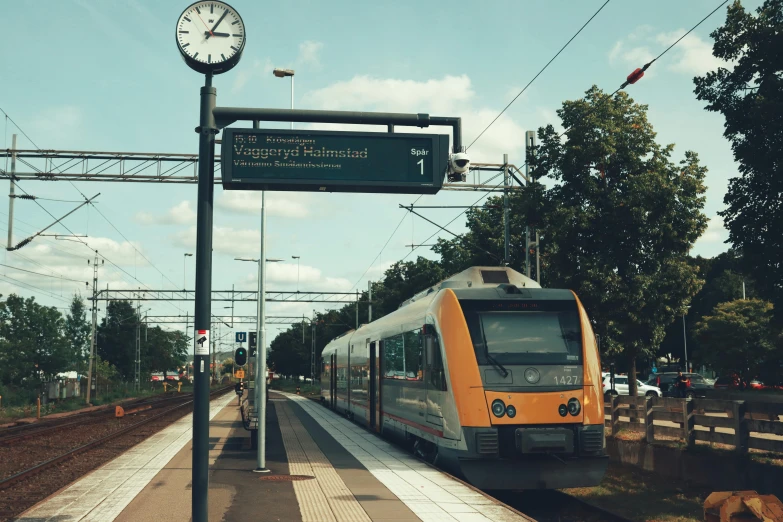 a very small commuter train at the station with a clock and warning sign