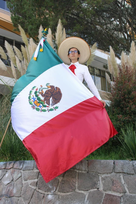 a man holding a mexican flag posing on a wall