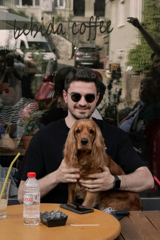 man sitting at a table holding his dog in front of the coffee shop