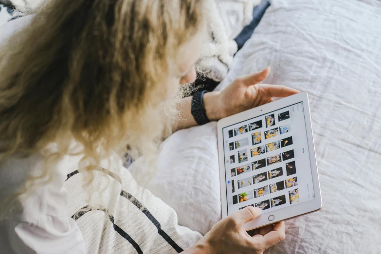 woman in bed holding an ipad looking at pos on the bed