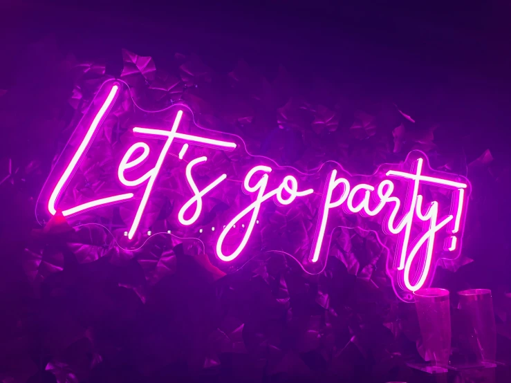 a neon sign reading let's go party is in front of dark vegetation