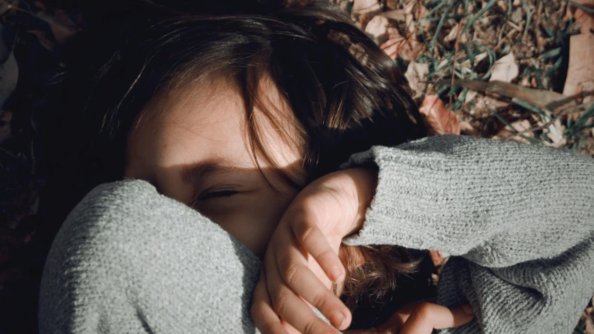 the young child covers her face with her arms