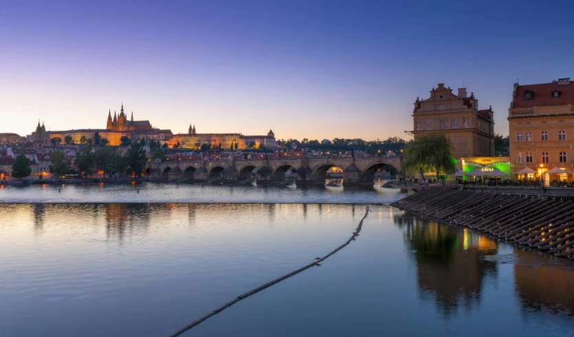 a stone bridge crossing across a river with a castle in the background