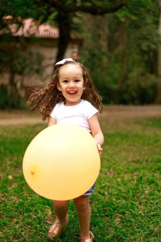 the girl holds a large yellow balloon in a park