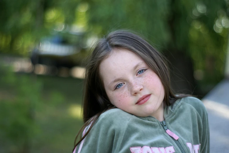 a girl in an sweatshirt sits next to a tree