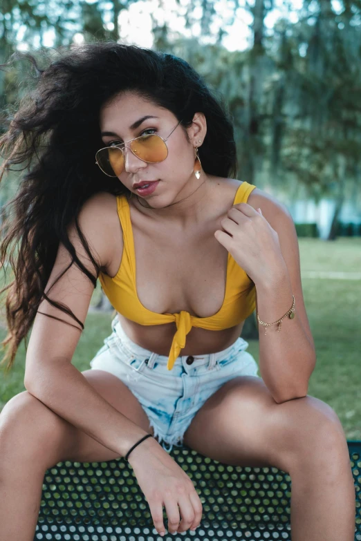 a young woman with dark hair in a yellow top and light blue denim shorts poses for the camera