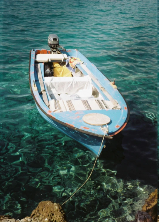 a blue boat with a man on it docked at a rock ledge